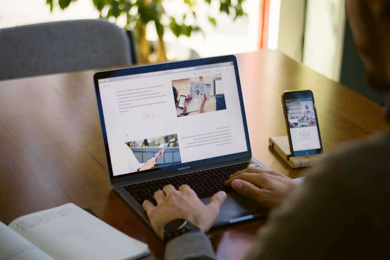 Someone working on a website on a laptop, with a smartphone on a stand beside it