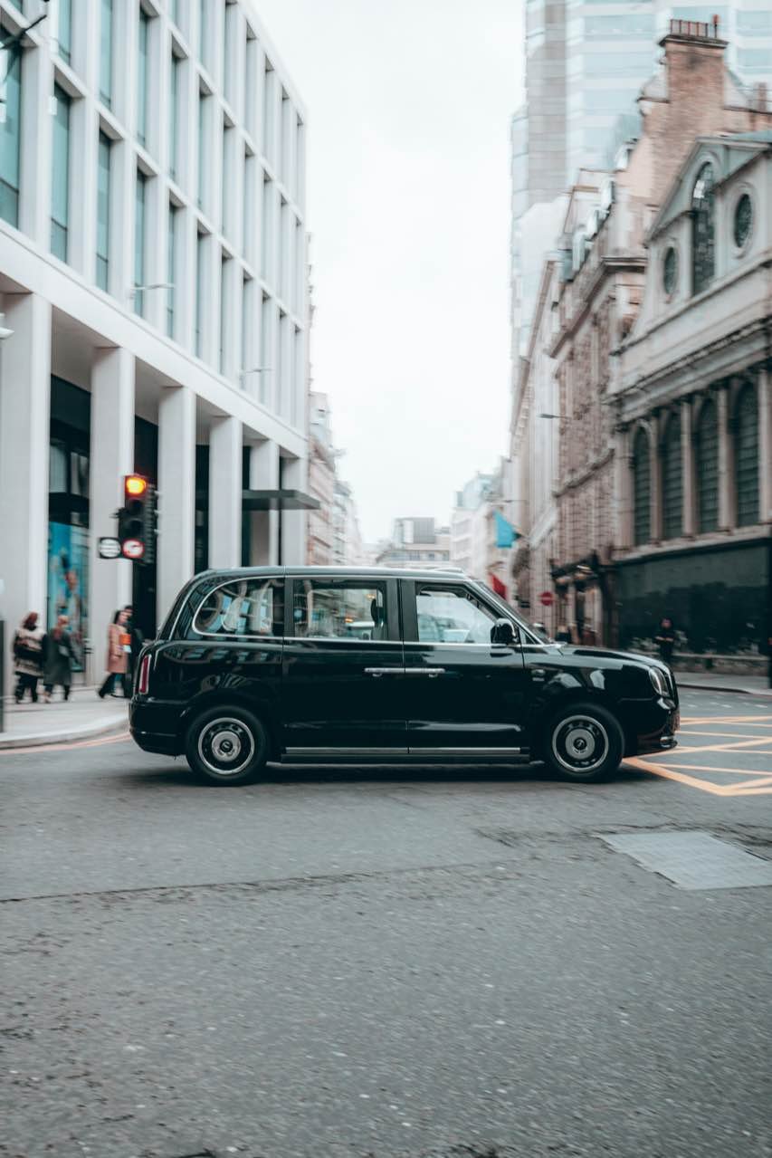 A black London taxi crossing a junction between office buildings on an overcast day