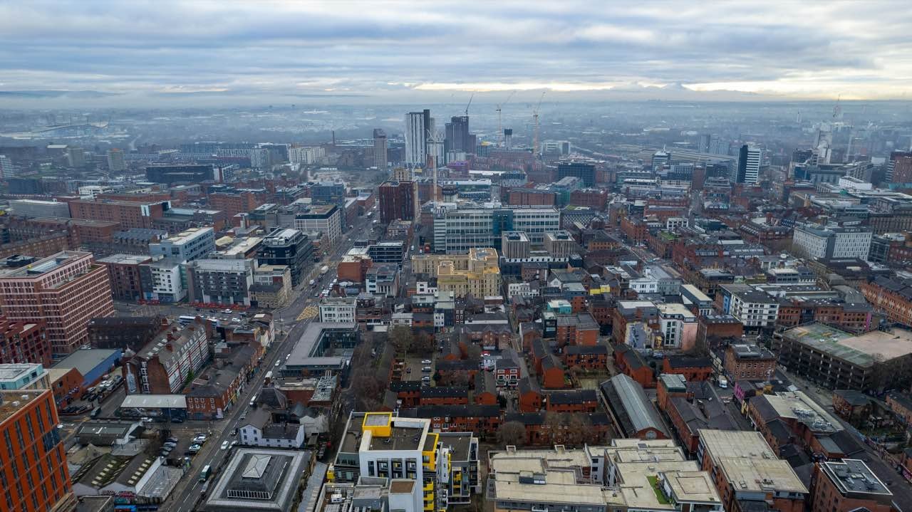 Aerial view of red-brick streets and modern buildings in a UK city under a cloudy sky