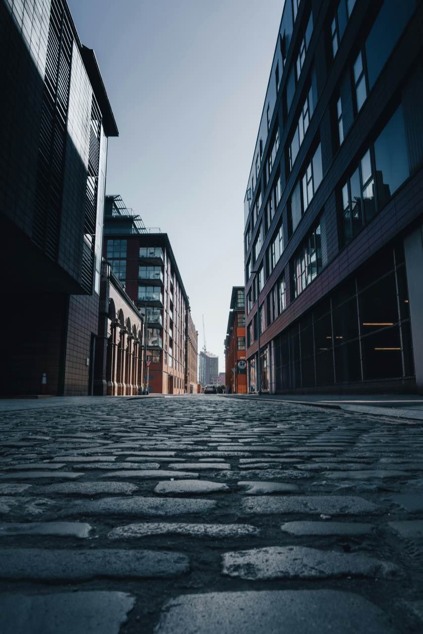 A cobbled city street between brick and glass buildings, seen from road level