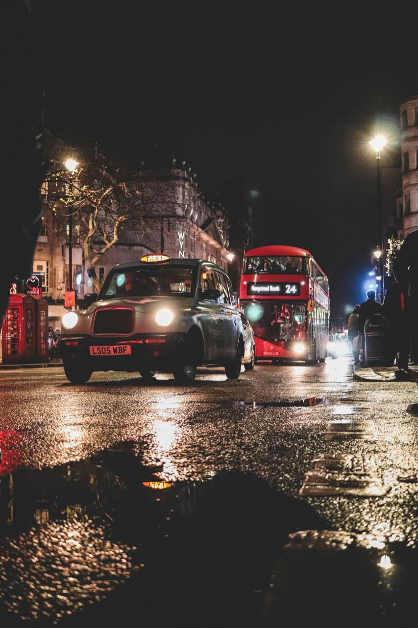 A black cab and a red double-decker bus on a wet London street at night