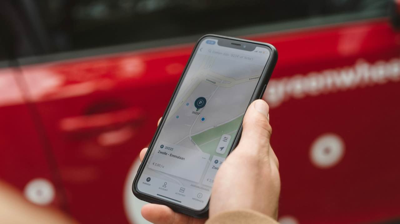 A hand holding a smartphone with a map app open, beside a red car