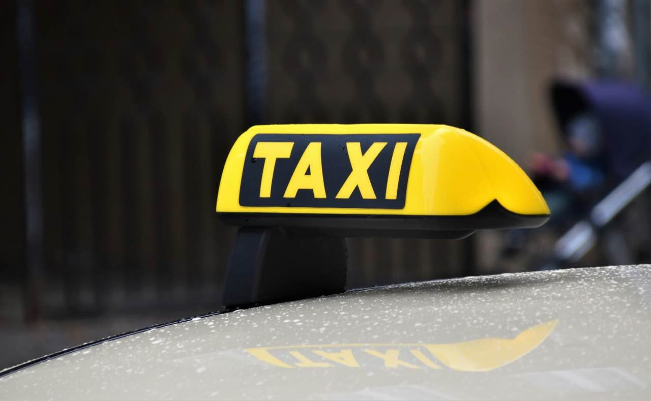 A yellow TAXI roof sign on a car, close up, with the street blurred behind